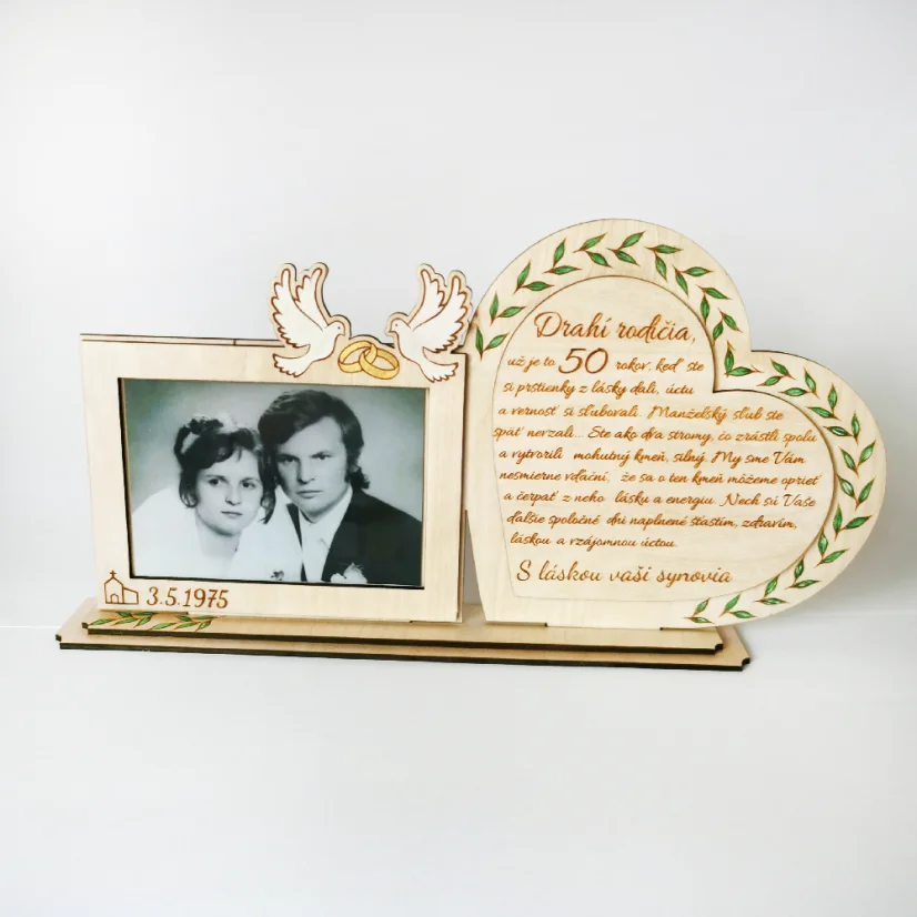 Drevená spomienková dekorácia s rámikovým miestom na svadobnú fotku. Vedľa v srdci gravírovaný text, po obvode srdca zelené maľované lístky. Na rámiku maľované biele holubice so zlatými obrúčkami, dole gravírovaný dátum svadby.