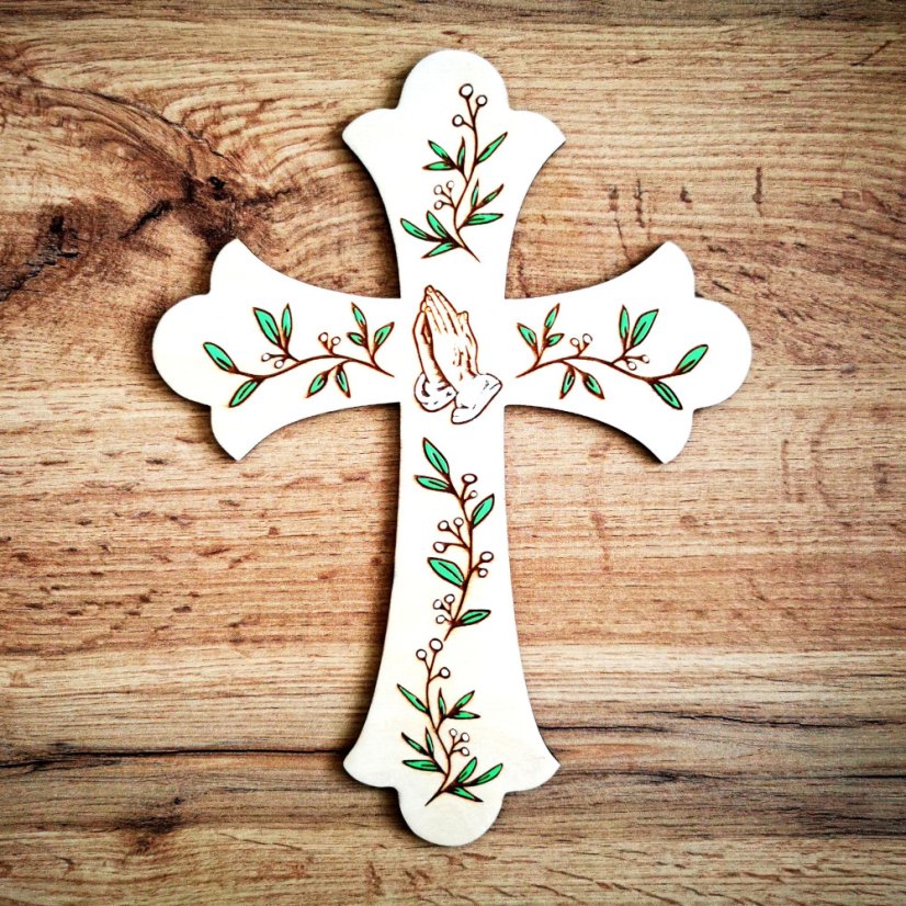 Drevený krížik na stenu s vygravírovanými modliacimi rukami a ručne maľovanými zelenými lístkami.