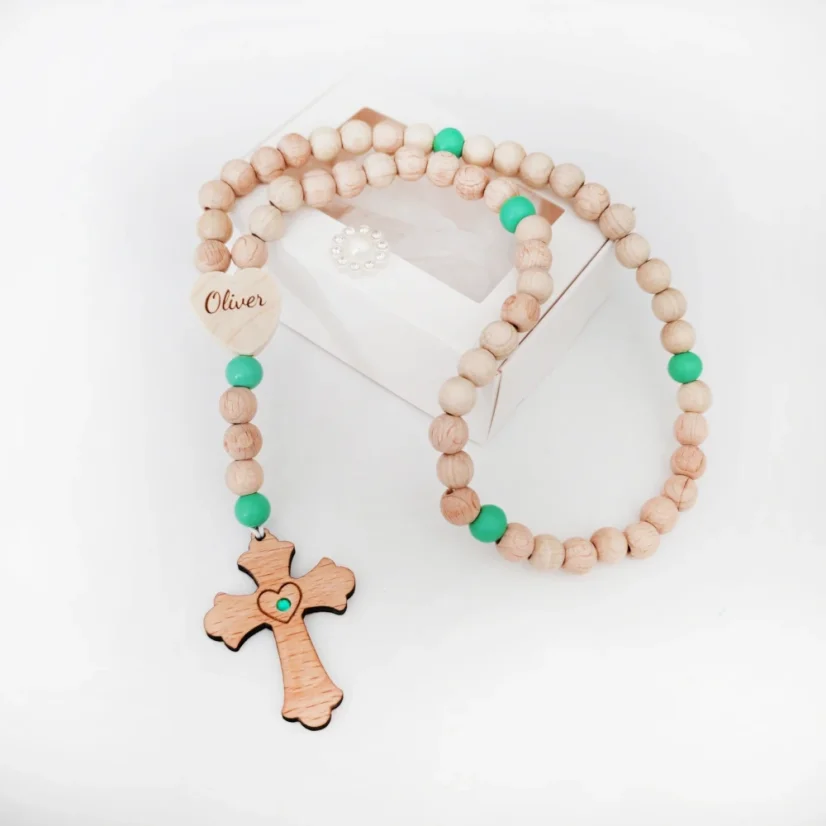 Ruženec s menom z bukových korálkov a krížiku, zelené mentolové desiatky z akrylu, v strede krížiku vložený kamienok vo farbe desiatkov. Ruženec položený na bielej darčekovej krabičke.