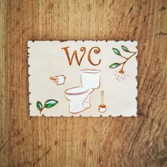 Drevená tabuľka na dvere s nápisom "WC", s gravírovanou a ručne maľovanou toaletou, toaletným papierom a kefou.