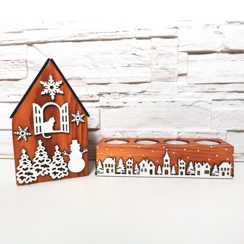 Drevený domček v hnedej lazúre s bielymi vianočnými výrezmi a k nemu zladený svietnik, ktorý je zdobený bielou zasneženou krajinkou kolom dokola.