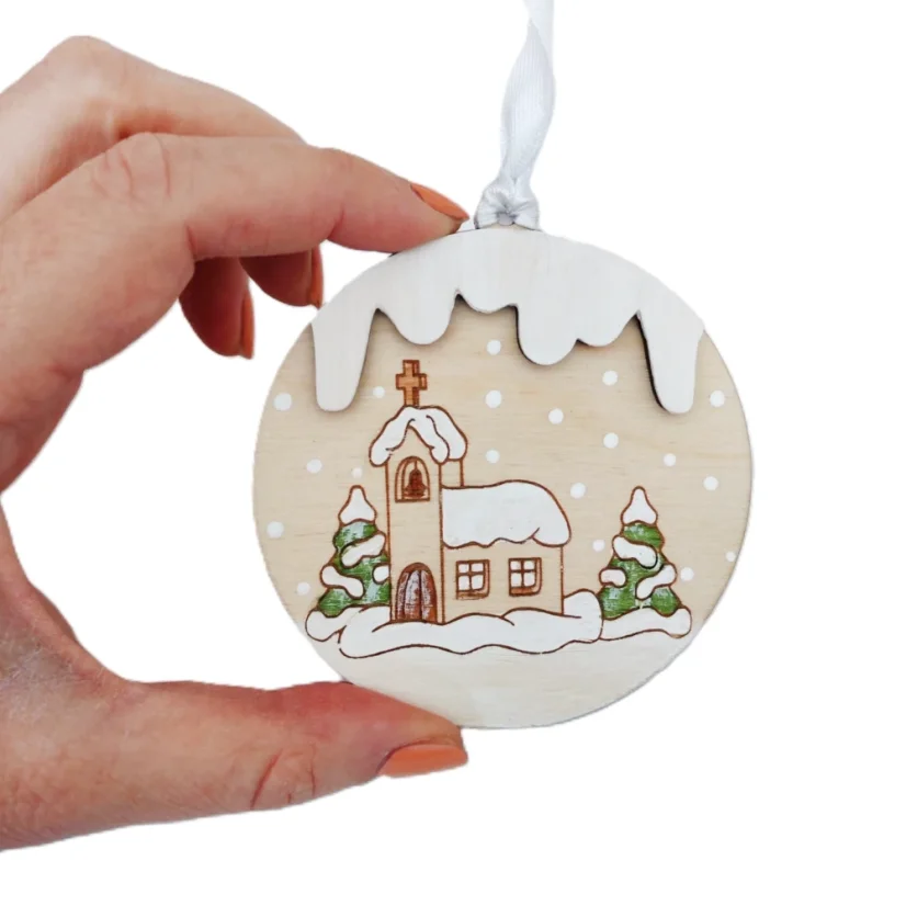 Drevená ozdoba na stromček s gravírovaným a ručne maľovaným zasneženým kostolíkom a ihličnatými stromami.