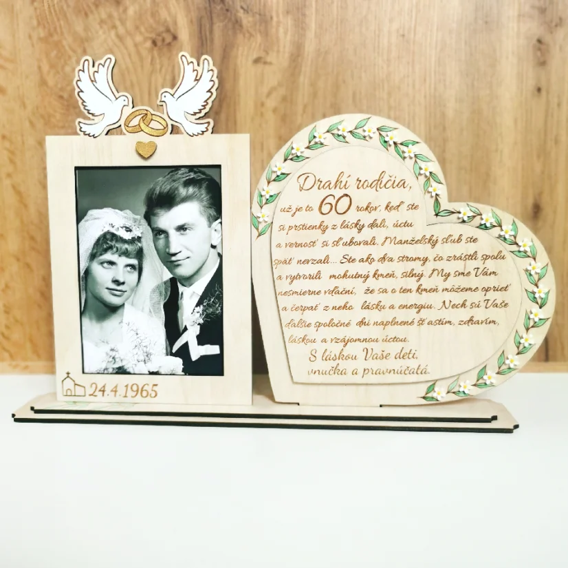 Drevená spomienková dekorácia s rámikovým miestom na svadobnú fotku. Vedľa v srdci gravírovaný text, po obvode srdca zelené maľované lístky dozdobené bielymi kvietkami z akrylu. Na rámiku maľované biele holubice so zlatými obrúčkami, dole gravírovaný dátum svadby.