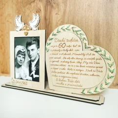 Drevená spomienková dekorácia s rámikovým miestom na svadobnú fotku. Vedľa v srdci gravírovaný text, po obvode srdca zelené maľované lístky dozdobené bielymi kvietkami z akrylu. Na rámiku maľované biele holubice so zlatými obrúčkami, dole gravírovaný dátum svadby.