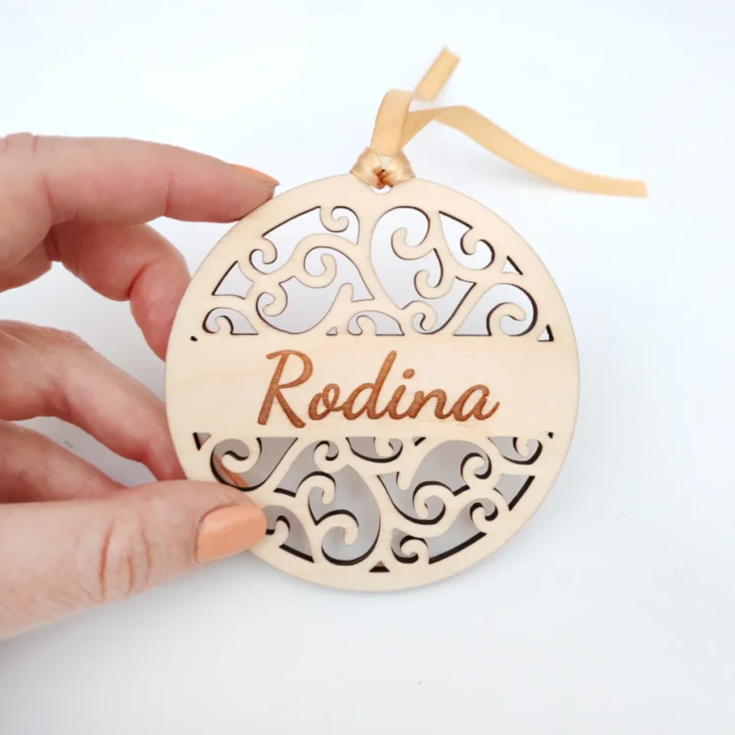 Detail drevenej vianočnej ozdoby s elegantným ornamentovým vzorom a s gravírovaným nápisom "Rodina".