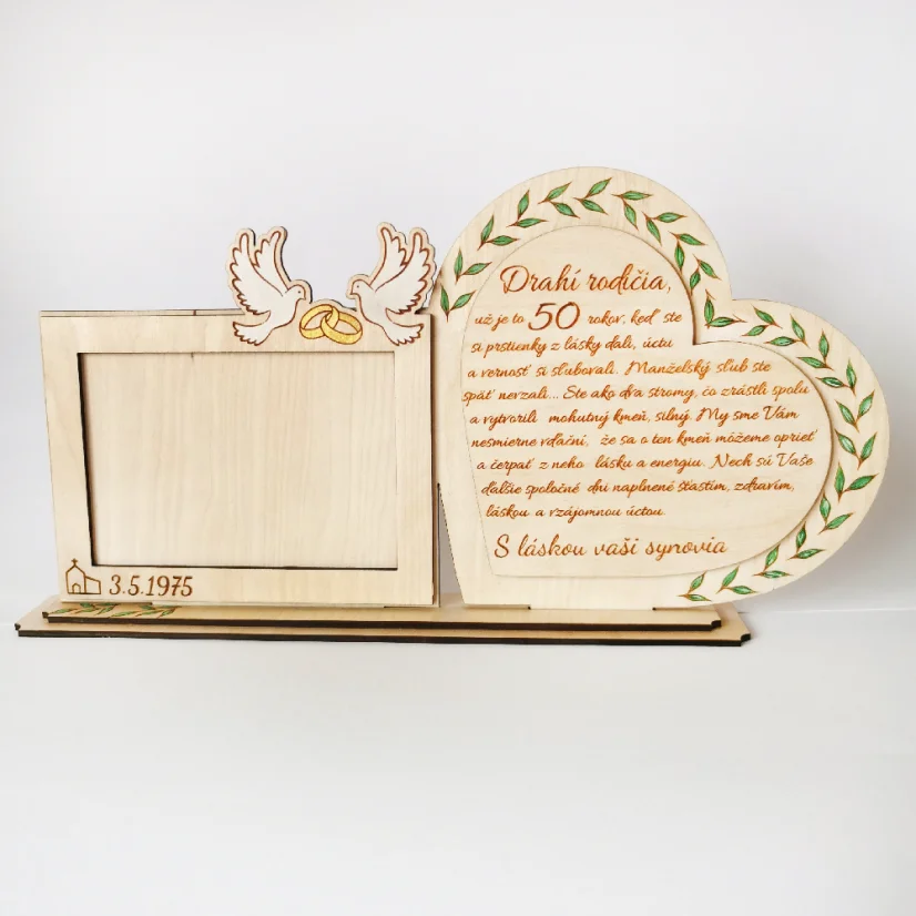 Drevená spomienková dekorácia s rámikovým miestom na svadobnú fotku. Vedľa v srdci gravírovaný text, po obvode srdca zelené maľované lístky. Na rámiku maľované biele holubice so zlatými obrúčkami, dole gravírovaný dátum svadby.