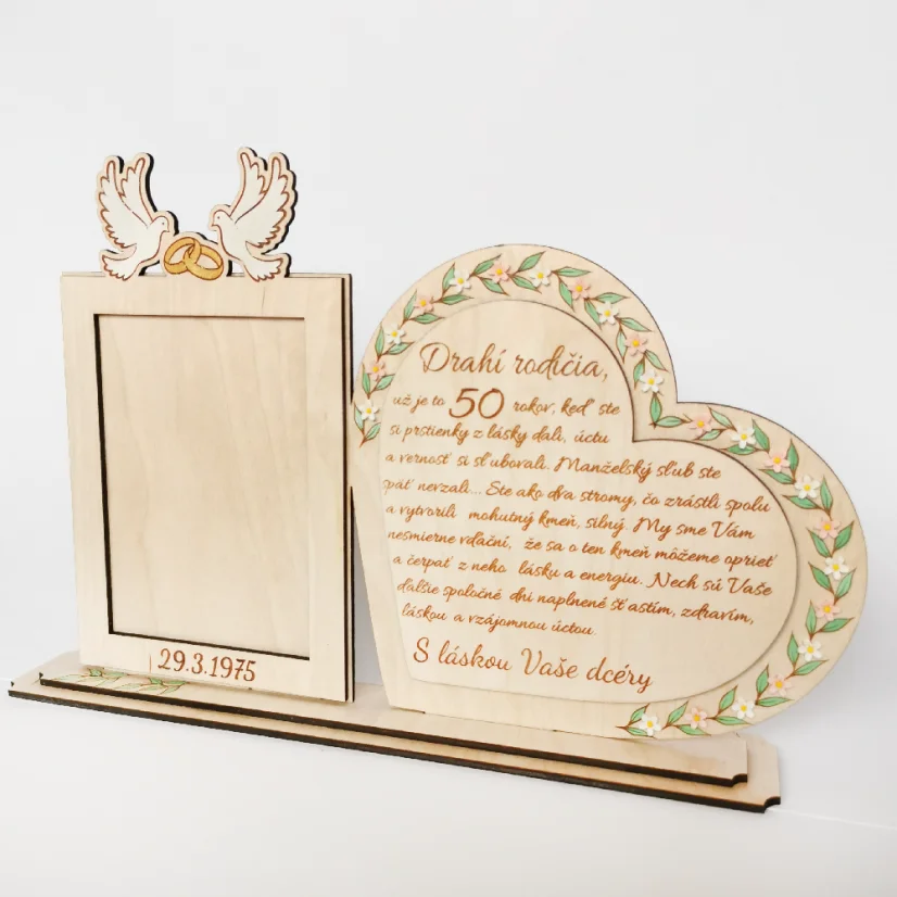 Drevená spomienková dekorácia s rámikovým miestom na svadobnú fotku. Vedľa v srdci gravírovaný text, po obvode srdca zelené maľované lístky dozdobené bielymi kvietkami z akrylu. Na rámiku maľované biele holubice so zlatými obrúčkami, dole gravírovaný dátum svadby.
