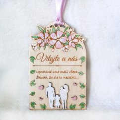 Drevená tabuľka s textom "Vitajte u nás, upratané sme mali včera, škoda že ste to nestihli", so siluetami postáv a s ručne maľovanými kvietkami a lístkami. 