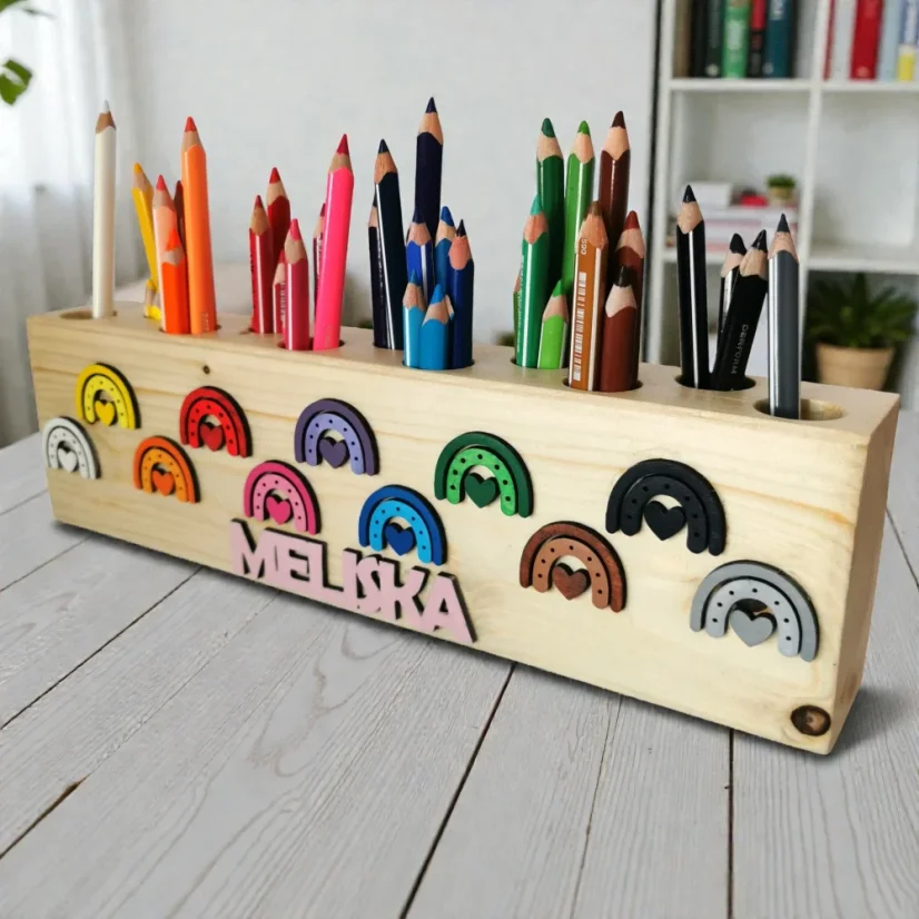 Drevený masívny pastelkovník s menom a roztriedenými pastelkami na stole.