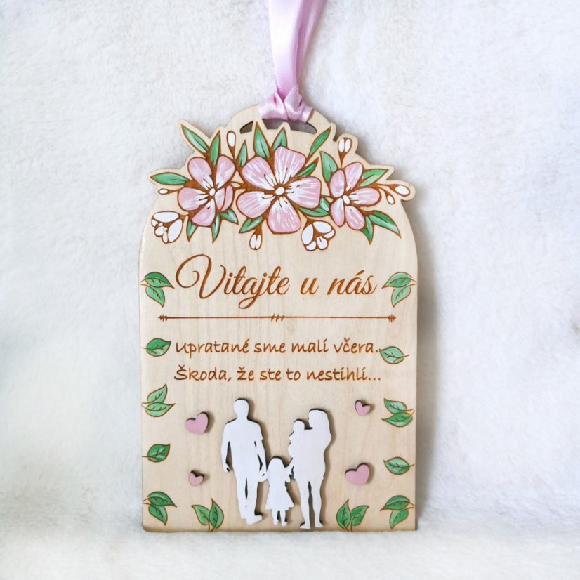 Drevená tabuľka s textom "Vitajte u nás, upratané sme mali včera, škoda že ste to nestihli", so siluetami postáv a s ručne maľovanými kvietkami a lístkami. 