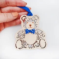 Drevená vianočná ozdoba v tvare medvedíka s modrou mašľou na krku a stuhou v rovnakej farbe. Drevená vianočná ozdoba v tvare medvedíka s modrou mašľou na krku a stuhou v rovnakej farbe.