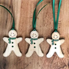 Tri drevené ozdoby perníčkov na stromček so zelenými šálmi a stuhou v červenej farbe. Tri drevené ozdoby perníčkov na stromček so zelenými šálmi a stuhou v červenej farbe.