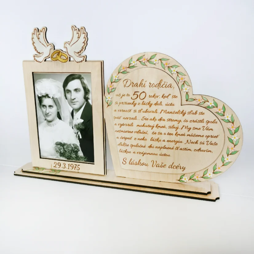 Drevená spomienková dekorácia s rámikovým miestom na svadobnú fotku. Vedľa v srdci gravírovaný text, po obvode srdca zelené maľované lístky dozdobené bielymi kvietkami z akrylu. Na rámiku maľované biele holubice so zlatými obrúčkami, dole gravírovaný dátum svadby.
